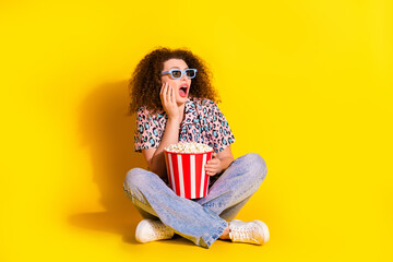 Young woman in stylish casual attire holding popcorn posing on yellow background expressing delight
