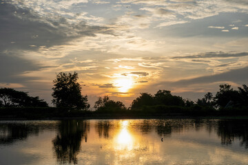 Sunset reflection over calm water with silhouetted trees and dramatic cloudy sky