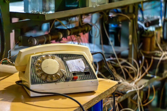 Vintage rotary dial telephone placed on a workbench in an electrical workshop. In the background, tangled wires, shelves with tools, and components create a retro technical setting.