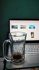 an empty glass of coffee standing on the laptop surface