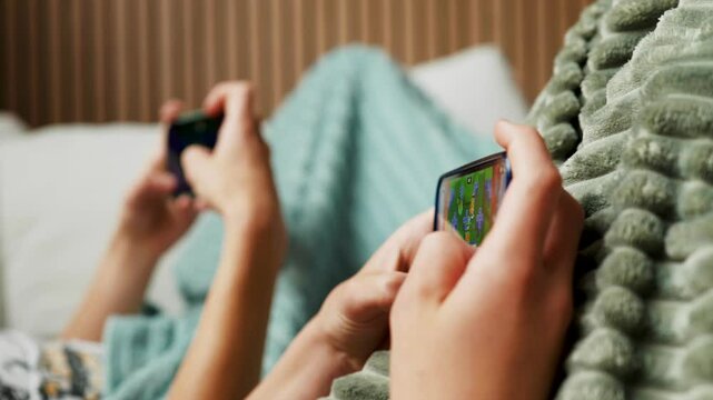 Close-up of hands, children playing mobile video games on smartphone on couch at home