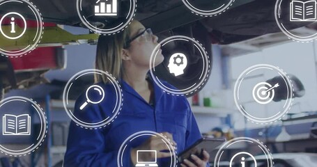 Auto technician tilting head under lifted car and tapping tablet as diagnostic icons appear logging - Powered by Adobe