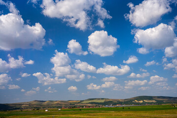 Fototapeta premium Expansive Rural Landscape with Rolling Hills and Scenic Cumulus Clouds in the Countryside of Mureș County, Romania
