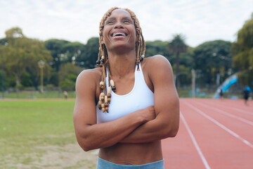 Portrait of a young African sportswoman on the court, arms crossed, laughing enthusiastically