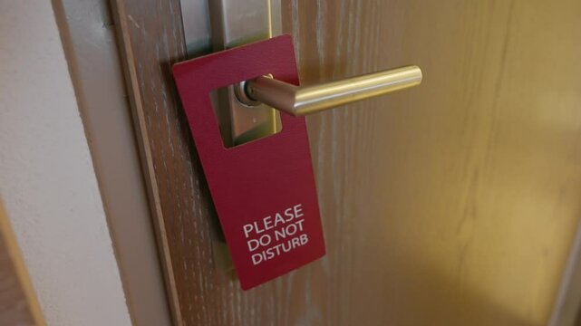 Female hand hangs a do not disturb door hanger sign in hotel suite or room. Woman guest in luxury hotel or tourist resort is requesting housekeeping no to enter or clean room. Privacy and quiet