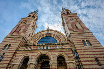 Fototapeta premium Low Angle View of the Holy Trinity Roman Catholic Church in Sibiu, Romania with Neo-Romanesque Architecture and Twin Bell Towers Against a Dramatic Sky