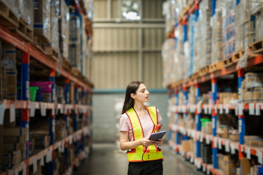Young White woman with barcode reader and tablet in large warehouse facility. Concept of smart warehouse, inventory tech, and industrial efficiency.