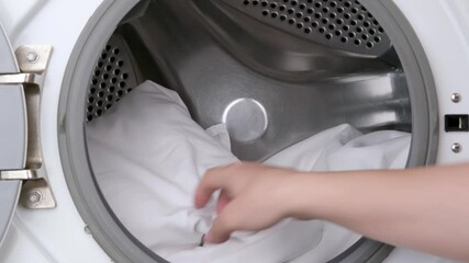 woman's hand putting white bed linen into washing machine - Powered by Adobe