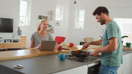 Young Couple Preparing Meal Together In Modern Kitchen Following Online Recipe On Laptop