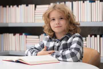 Fototapeta premium Child reading a red book in the library. Little student on school library.