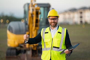 Construction manager in suit and helmet at a construction site. Construction manager worker or supervisor wearing hardhat in front of house. Supervisor construction manager near excavator. Renovation.