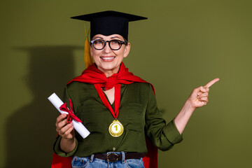 Charming mature woman in graduation cap and cloak holding certificate, wearing a medal, smiling and...