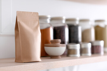 A blank pouch sits on a wooden shelf in a minimal pantry surrounded by jars and spices, showcasing a clean and organized kitchen vibe