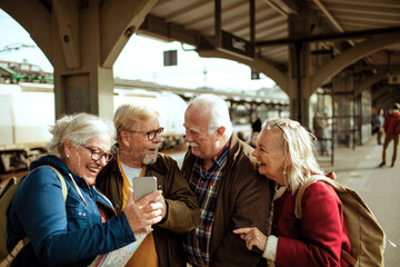 Senior friends laughing at phone while waiting at train station