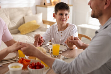 Family praying together before dinner at table indoors