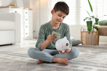 Boy putting pocket money into piggybank at home