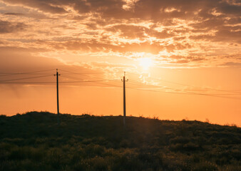 Obraz premium Sunset over rural landscape with power lines silhouetted against golden sky.