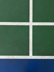 Top-down view of a badminton court section showing green and blue flooring with white boundary lines. The minimal and geometric composition makes it ideal for sports backgrounds and design elements.