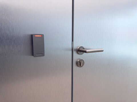 Close up of metal door with handle and electronic card reader. Concept of restricted access, modern security systems, staff area control and building access technology
