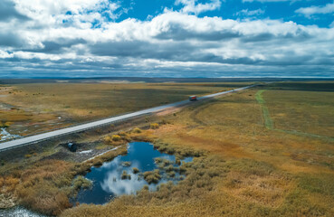 Aerial view of a truck navigates a long, winding road surrounded by expansive fields and gentle hills.
