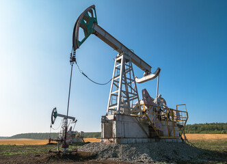 Oil pumps operate in a vast field under a clear blue sky at midday in rural area