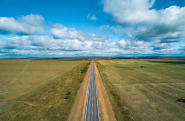 Vast open landscape with a long straight road stretching through the fields under a blue sky
