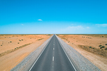 Stretch of highway through barren desert landscape under clear blue sky in remote location