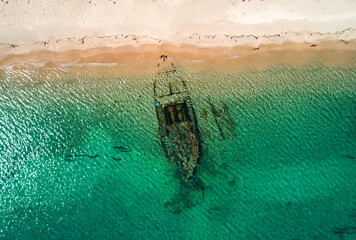 Shipwreck partially submerged in clear turquoise water along a sandy beach during daylight