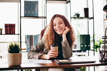 Confident Professional Woman at Workspace in Stylish Office Interior Holding Coffee