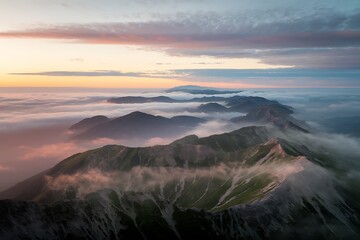 Obraz premium Aerial view of mountain range with fog and clouds at sunrise, showcasing a serene and majestic landscape with a dreamy and ethereal atmosphere