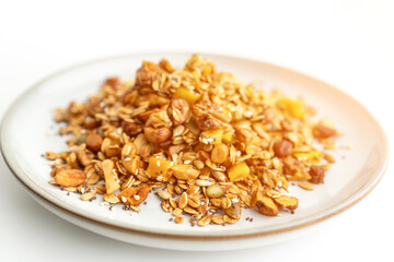 A bowl of granola with nuts and seeds on a white plate. The granola is a mix of different types of grains and nuts, and it looks like a healthy snack.