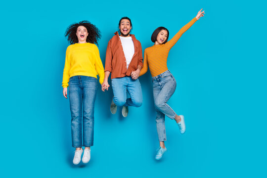 Three friends jumping joyfully against a blue background showcasing diversity, friendship, and happiness in a casual lifestyle
