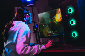 Young female gamer immersed in online video game streaming with neon lights and a vibrant computer...