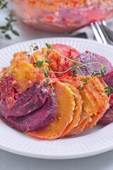 Sweet potato, parsnips and beet root gratin with thyme and melted cheese, on white plate, vertical