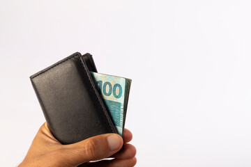 a man's hand holding a wallet with Brazilian 100 reais notes