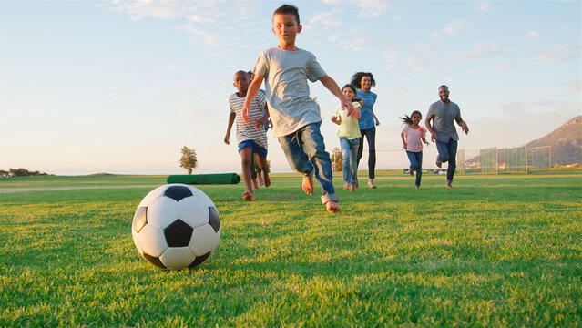 Multi Cultural Families Having Fun Playing Soccer In Park With Evening Light