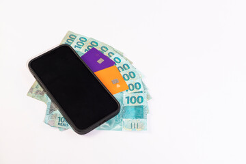 Black Cell Phone, credit cards and Brazilan 100 Reais Banknotes on a white background