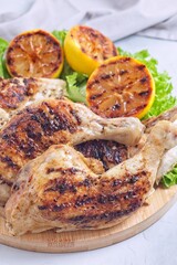 Grilled chicken legs and breast with lemon and lettuce on wooden board, vertical