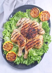 Spatchcocked grilled chicken with lemon garlic marinade on lettuce with lemon, vertical top view