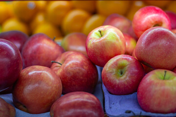 Fresh red apples displayed on a market stall with oranges in the background