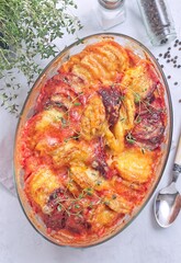 Gratin with sweet potato, parsnips, beet root and melted cheese, in glass dish, vertical top view