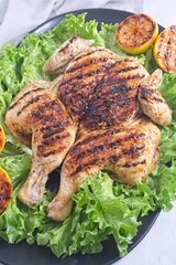 Grilled spatchcocked chicken with lemon garlic marinade on lettuce with lemon halves, vertical