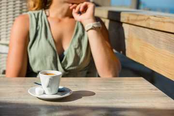 Beautiful young woman enjoying an espresso served on a terrace with the ocean in the background.