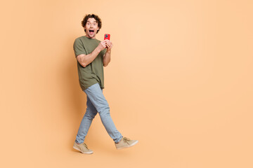 Excited young man holding smartphone and expressing joy on beige background wearing casual khaki...