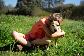 Boy hugging his dog in a green meadow on a sunny day