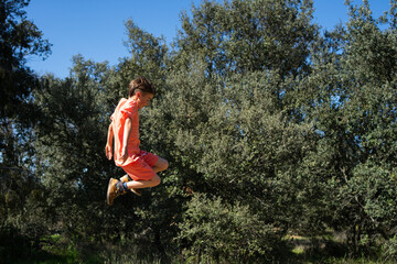 Boy jumping outdoors in a forest wearing orange clothes