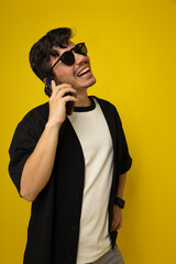 Vertical image of a young freckled man with a mustache happily talking on his smartphone on a yellow background with space for advertising