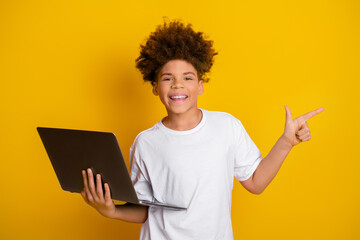 Smiling boy holding laptop and gesturing on bright yellow background showcasing cheerful learning and confidence