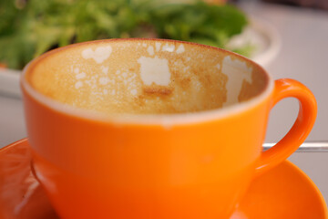 Empty orange coffee cup with remnants at cafe table