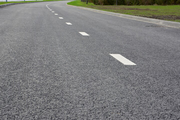 Obraz premium Curving asphalt road with white lane markings close up